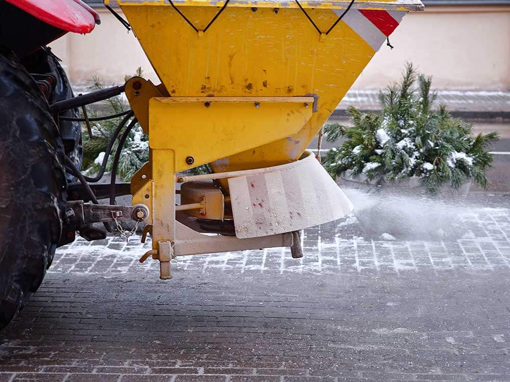 Tractor de-icing street, spreading salt on footpath